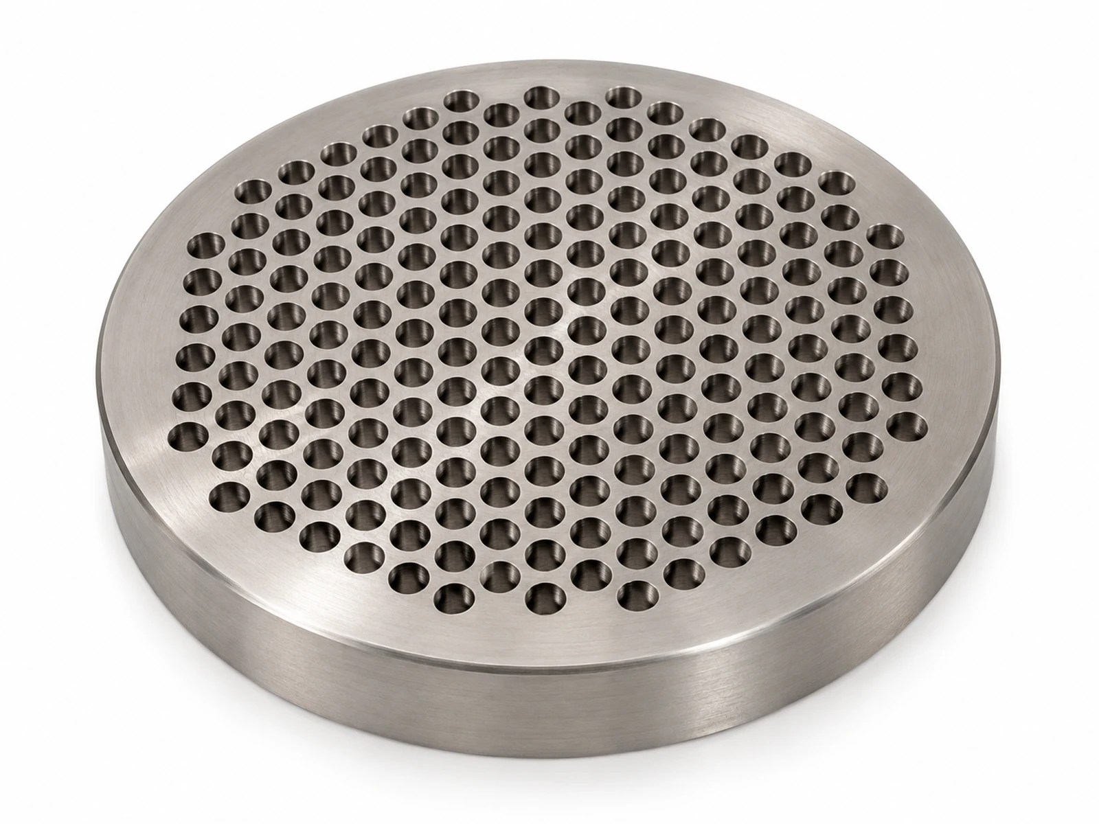 A thick round stainless steel extruder breaker plate with many evenly spaced drilled holes, resting on a workbench
