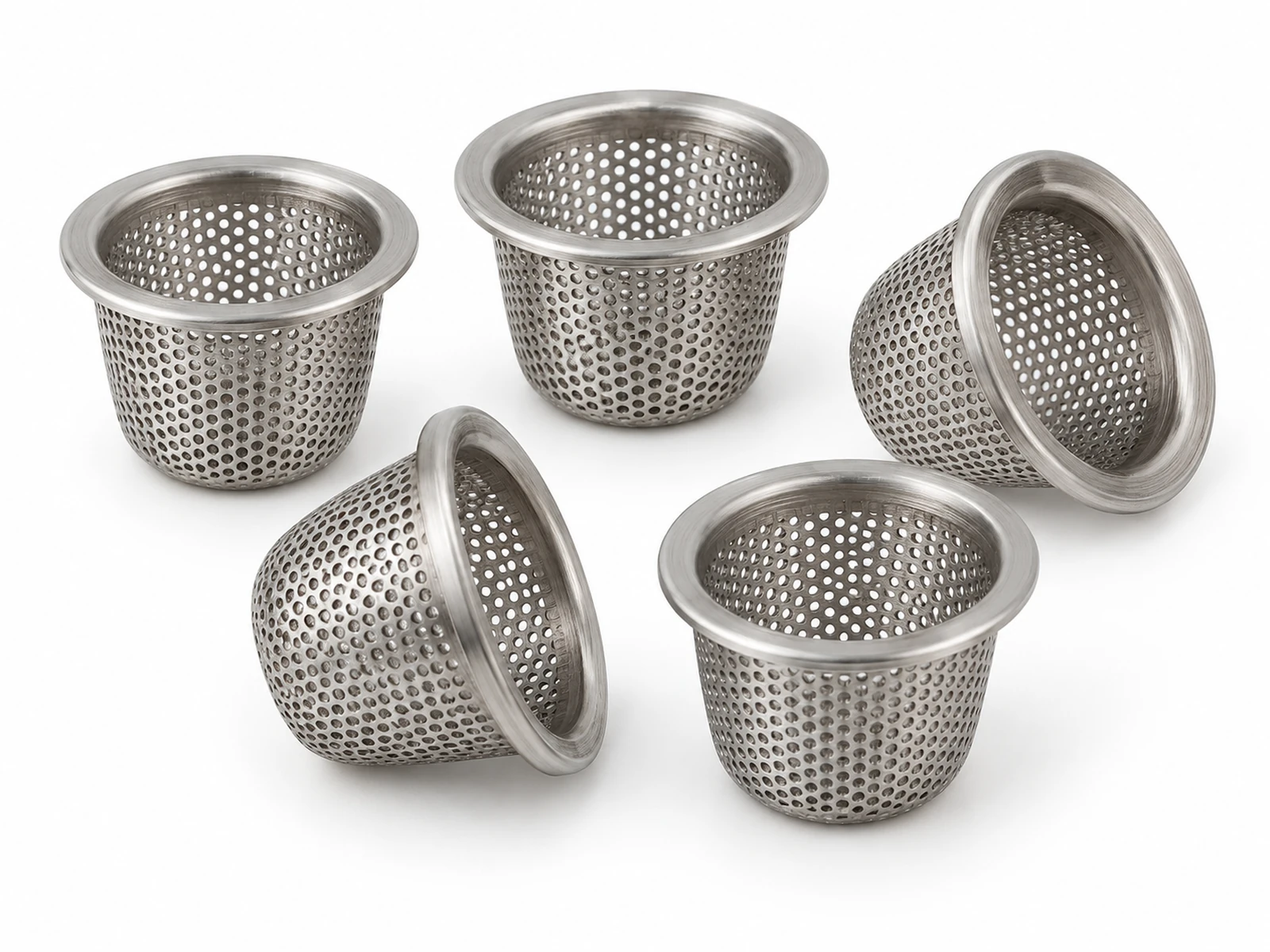 Several tiny cup-shaped stainless steel filters formed from etched foil with visible micro holes, on a fingertip for scale