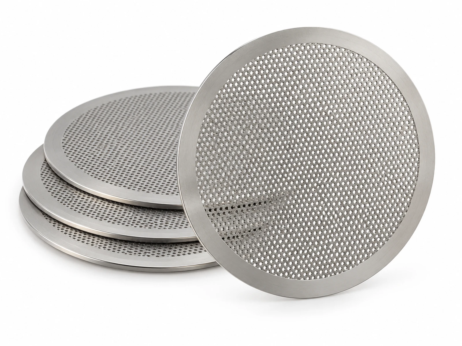 Several thin photo-etched stainless steel filter discs with fine uniform hole patterns, one held up to light