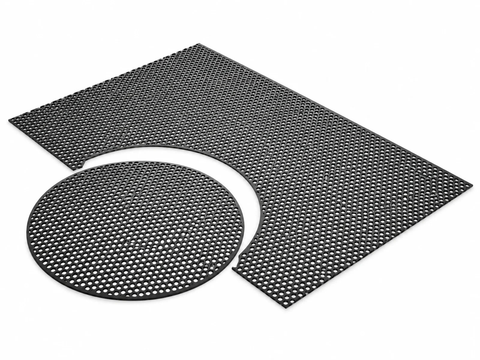 A large black perforated metal speaker grille sheet partly cut into a round grille with tin snips, a speaker cabinet